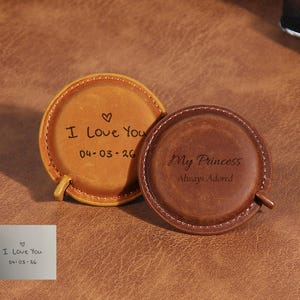 Può includere: Due metri a nastro rotondi in pelle con bordi cuciti. Il nastro color cuoio chiaro è inciso con un cuore, "I Love You" e "04-03-26". Il nastro marrone scuro è inciso con "My Princess" e "Always Adored". Un piccolo cartoncino bianco mostra il testo.