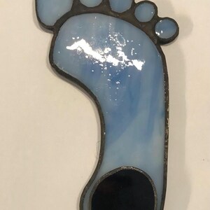 Puede incluir: Un adorno de pie de vidrio azul tintado con un c&iacute;rculo negro en el centro. El pie est&aacute; bordeado de negro y tiene un peque&ntilde;o lazo en la parte superior para colgar.