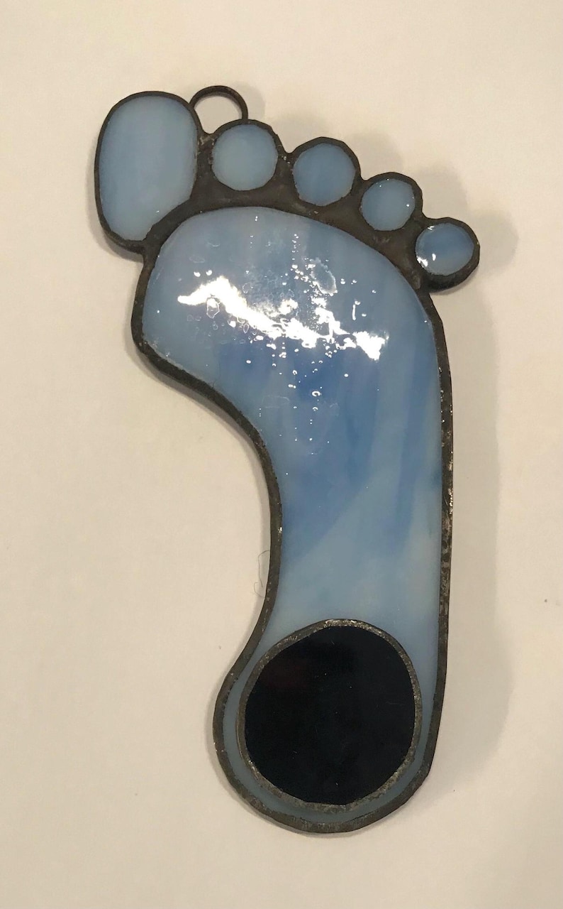 Puede incluir: Un adorno de pie de vidrio azul tintado con un c&iacute;rculo negro en el centro. El pie est&aacute; bordeado de negro y tiene un peque&ntilde;o lazo en la parte superior para colgar.