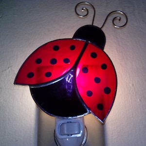May include: A ladybug night light with a red and black design. The ladybug's wings are red with black spots, and the body is black. The night light has a white base and a switch.