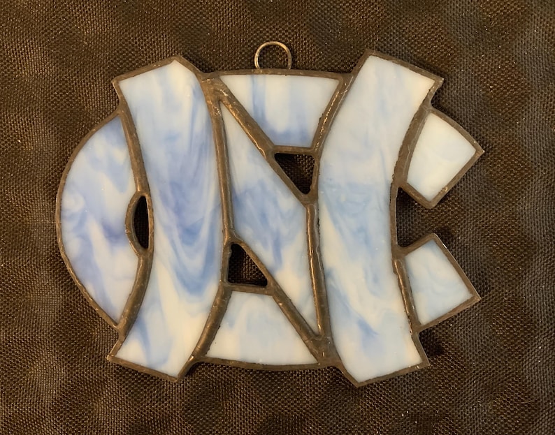 Peut inclure: Une d&eacute;coration en verre teint&eacute; repr&eacute;sentant les lettres "UNC" en bleu et blanc.