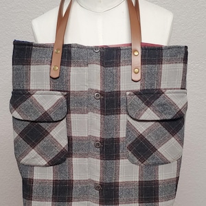May include: A gray and white plaid tote bag with brown leather straps and two large pockets. The bag is made from repurposed flannel.