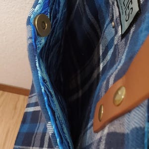 May include: A blue and white plaid tote bag with a brown leather strap and a blue velvet lining. The bag has a magnetic closure and a label that says "Woolies by Christel".