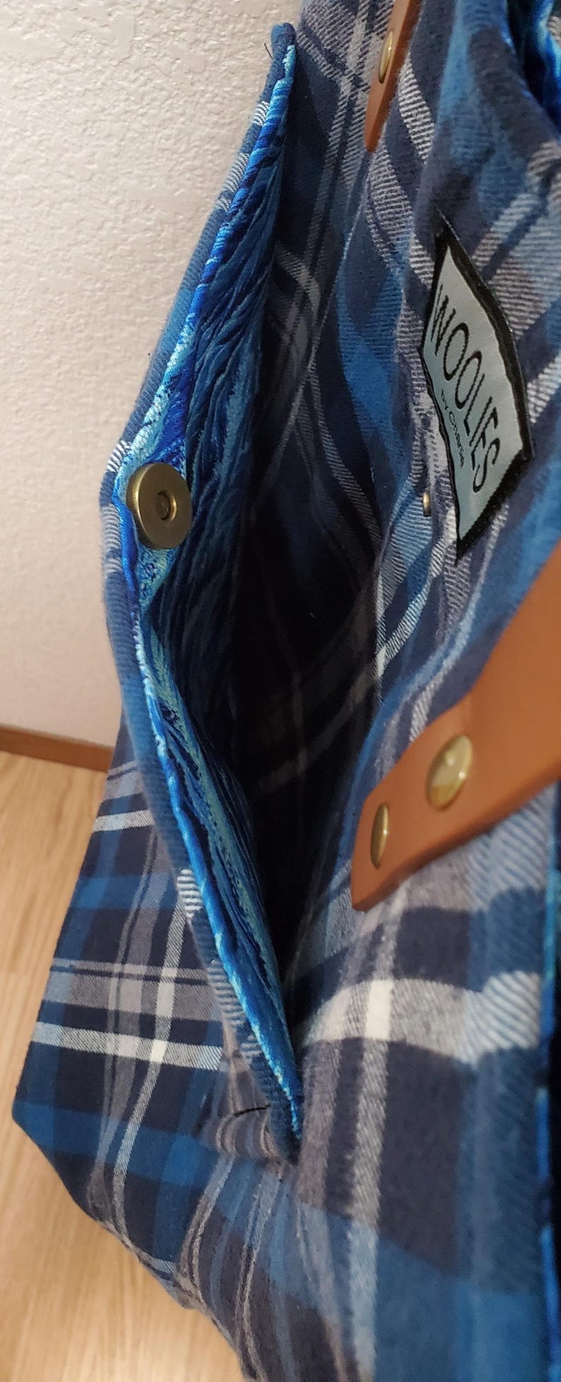 May include: A blue and white plaid tote bag with a brown leather strap and a blue velvet lining. The bag has a magnetic closure and a label that says "Woolies by Christel".