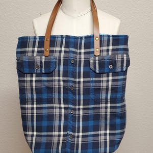 May include: A blue and white plaid tote bag with brown leather straps and gold-toned hardware. The bag has two large pockets on the front.