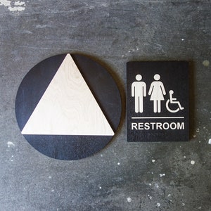 May include: Black and white restroom sign with a triangle symbol and the word "RESTROOM" on a black background.