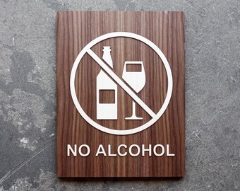 May include: A brown wooden sign with a white circle and a diagonal line through it. Inside the circle are images of a bottle and a wine glass. The text "NO ALCOHOL" is printed below the circle.