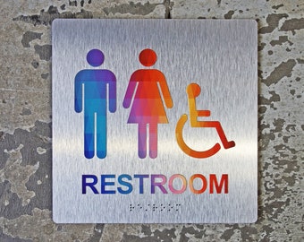 May include: A silver metal sign with a rainbow-colored restroom symbol. The sign includes a male, female, and wheelchair accessibility symbol. The text "RESTROOM" is also included in rainbow colors.
