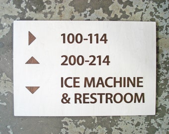 May include: White sign with brown text and arrows indicating directions to floors 100-114, 200-214, and the ice machine and restroom.