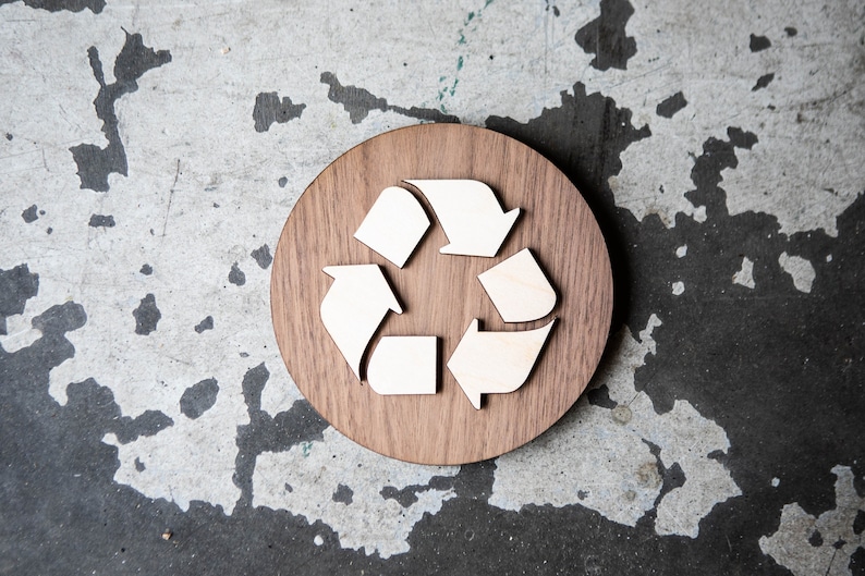 May include: A wooden round sign with a white recycle symbol in the center. The sign is made of dark wood and has a natural grain pattern.