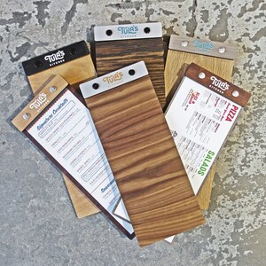May include: Five wooden menu boards with metal clips and the text "Tula's Kitchen" on each. The boards are arranged in a semi-circle on a gray concrete surface. The menus include "Signature Cocktails", "Salads", "Pizza", and "Specials".