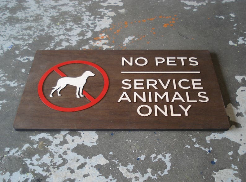 May include: A brown wooden sign with white text that reads "No Pets Service Animals Only". A red circle with a white silhouette of a dog is in the upper left corner of the sign.