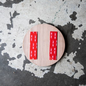 May include: A round piece of wood with two strips of red 3M tape attached to the back.