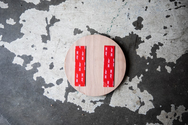 May include: A round piece of wood with two strips of red 3M tape attached to the back.