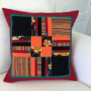 Peut inclure: Un oreiller rouge avec une bordure turquoise et un motif patchwork. Le patchwork comprend des tissus noirs, orange et jaunes avec des motifs floraux.