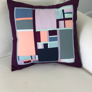 Peut inclure: Un oreiller violet avec un motif géométrique dans des tons de rose, bleu, gris et blanc.