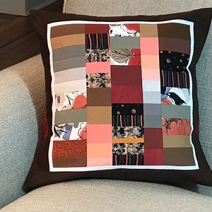 May include: A brown and white patchwork cushion with a variety of patterns and colours, including red, pink, green, and black.