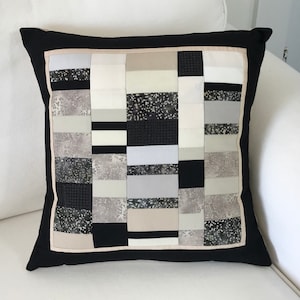 May include: Black and white geometric patterned cushion with a black border. The cushion is made of different fabrics with a variety of textures.
