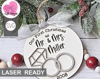 Puede incluir: Adorno navideño de madera blanca con el texto "Our First Christmas as Mr. & Mrs. Miller" y el año 2008. El adorno presenta un anillo de diamantes y dos anillos de boda. Se adjuntan una cinta plateada y una cuerda para colgar.