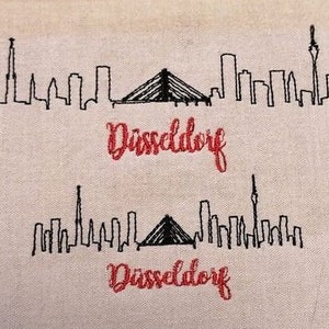 Puede incluir: Dos imágenes bordadas en blanco y negro del horizonte de Düsseldorf con la palabra "Düsseldorf" bordada en rojo debajo de cada imagen.
