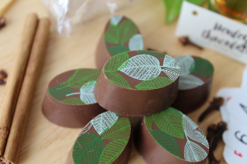 May include: A close-up of five chocolate truffles with a green and white leaf design. The truffles are arranged in a pile on a wooden surface.