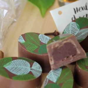 May include: Assortment of chocolate truffles with a green and white leaf design. The truffles are arranged on a wooden surface. Henley Chocolates is printed on a white tag.