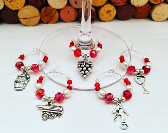 May include: Wine glass charms with red, white, and clear beads. Each charm has a silver-toned wine-themed pendant, including a barrel, grape cluster, wine bottle, corkscrew, and wine glass. The charms are designed to hang on a wine glass.