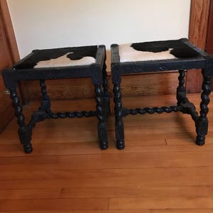 May include: Two black wooden stools with a cowhide seat. The stools have a twisted leg design.