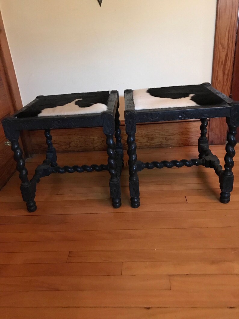 May include: Two black wooden stools with a cowhide seat. The stools have a twisted leg design.