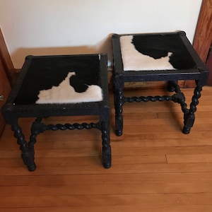 May include: Two black wooden stools with a black and white cowhide seat. The stools have a twisted leg design.