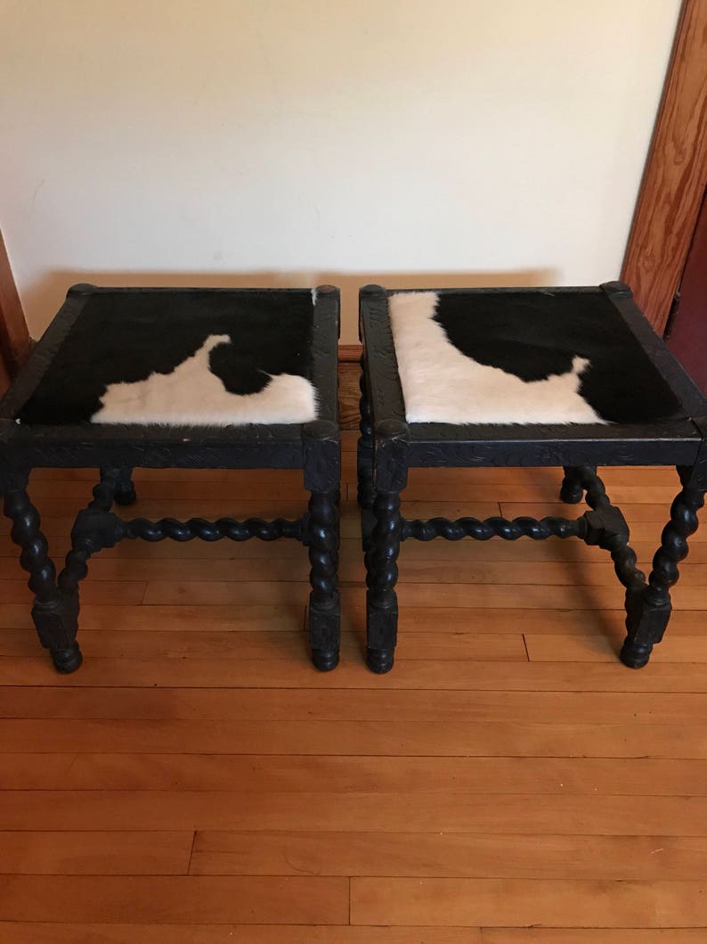 May include: A pair of black wooden stools with twisted legs and cowhide seats. The cowhide is black and white.