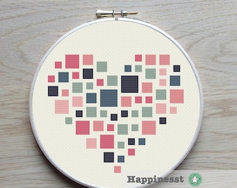 Puede incluir: Un patrón de punto de cruz de un corazón hecho de cuadrados rosas, verdes y azules. El corazón está centrado en un fondo blanco y está rodeado por un aro de bordado de madera.