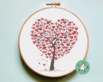 Puede incluir: Un aro de bordado de punto de cruz con un árbol en forma de corazón hecho de corazones rosas y rojos. El árbol tiene un tronco y ramas marrones. El fondo es blanco.