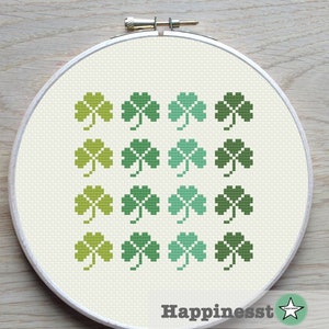 May include: A cross-stitch pattern featuring a gradient of green shamrocks. The shamrocks are arranged in four rows of four, with the lightest green shamrocks at the top and the darkest green shamrocks at the bottom.