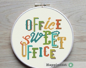 May include: A cross-stitch embroidery hoop with the words "OFFICE SWEET OFFICE" in colorful letters. The text is in a variety of fonts and colors, including orange, green, and teal. The background is a light cream color.