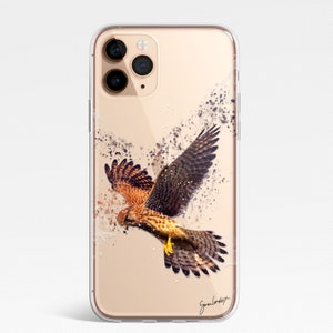 May include: Clear phone case featuring a watercolor illustration of a hawk in flight. The artwork showcases the bird with brown and tan feathers, wings spread, and dark ink splatter effects. The case has a glossy finish and a signature in the bottom right corner.