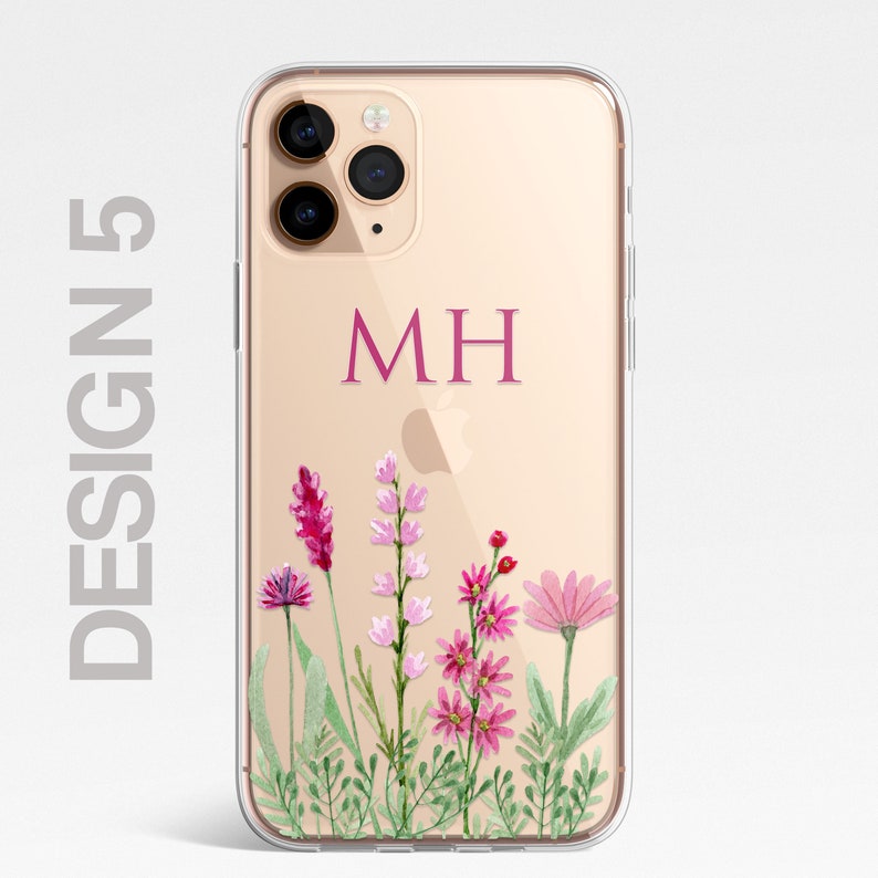 Op de afbeelding: Een transparante telefoonhoes met een gouden achtergrond en een bloemenontwerp. De hoes heeft een roze monogram "MH" op de achterkant.