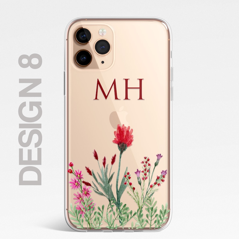 Op de afbeelding: Een transparante telefoonhoes met een gouden achtergrond en een bloemenontwerp. De hoes heeft een rode bloem met groene bladeren en roze bloemen. De initialen "MH" zijn in rood op de hoes gedrukt.