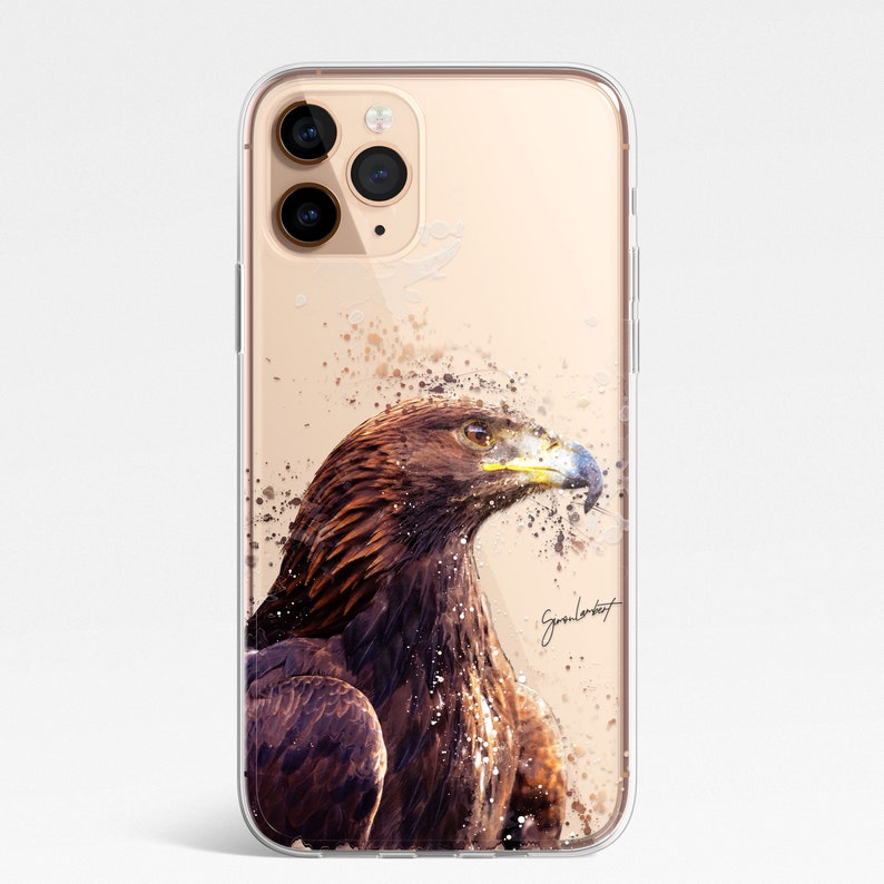 May include: Clear phone case featuring a watercolor painting of a brown eagle with a yellow beak and blue accents. The design includes paint splatter effects and a signature in the bottom right corner. The case is designed for a smartphone.