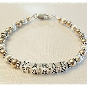 May include: A silver and gold beaded bracelet with the name "FARAH" spelled out in silver block letters.