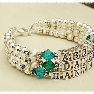 May include: Silver bracelet with teal beads and silver charm beads spelling out the names Abby, Dale, and Hanna.