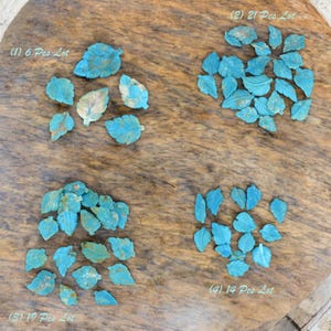 Puede incluir: Cuatro lotes de cuentas talladas en forma de hoja de turquesa se muestran sobre una superficie de madera. Los lotes están etiquetados (1) 6 Pcs Lot, (2) 21 Pcs Lot, (3) 19 Pcs Lot y (4) 14 Pcs Lot. Las hojas tienen vetas detalladas y color azul-verdoso.