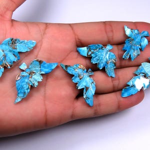 Può includere: Sette ciondoli a forma di foglia turchese con venature color oro sono esposti in una mano. Le foglie hanno un aspetto a mosaico, con diverse sfumature di blu e oro. Questi ciondoli sono ideali per la creazione di gioielli.