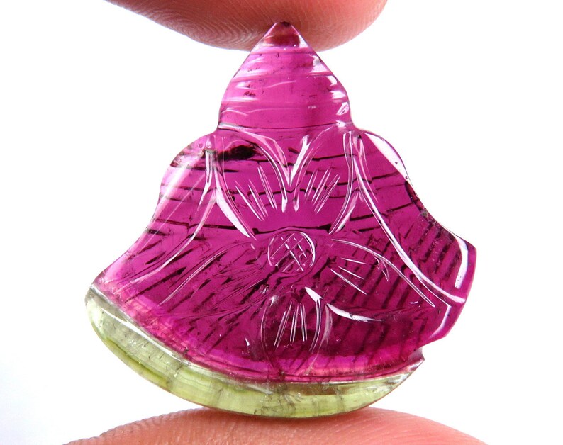 May include: A carved gemstone in a flower shape, featuring a vibrant color gradient. The top is a deep pink, transitioning to a lighter pink and then to a green base. Intricate lines and a floral design are carved into the stone.