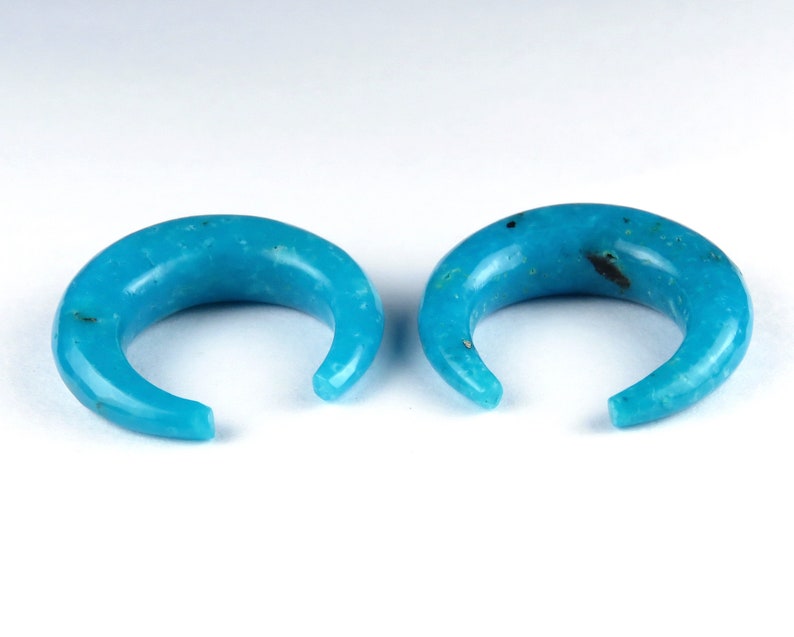 May include: A pair of turquoise crescent-shaped ear gauges. The gauges are smooth and polished, with a curved design. The open ends are rounded. The background is white. Each gauge is approximately 2.5 cm in diameter.