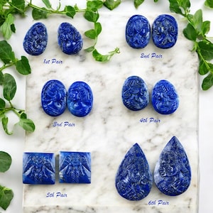 May include: Six pairs of carved lapis lazuli earrings, each pair featuring a different design. The earrings are displayed on a white marble surface with green foliage.