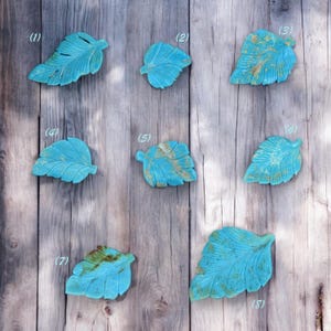 May include: Eight turquoise leaf-shaped decorative pieces with varying patterns and textures. The leaves are arranged in rows on a wooden background.