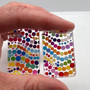 May include: Two rectangular, clear acrylic pieces with colorful polka dot patterns. The dots are in various sizes and colors, including red, orange, yellow, green, blue, and purple. The pieces are held up against a white background.