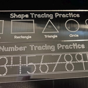 May include: Two clear acrylic tracing boards. The top board says "Shape Tracing Practice" and features dotted outlines of a square, rectangle, triangle, circle, and heart. The bottom board says "Number Tracing Practice" and has dotted numbers 1-10.