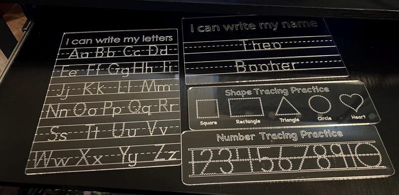 May include: Clear acrylic learning boards for writing practice. Includes boards for letters, name, shapes, and numbers. The text "I can write my letters", "I can write my name", "Shape Tracing Practice", and "Number Tracing Practice" are visible.